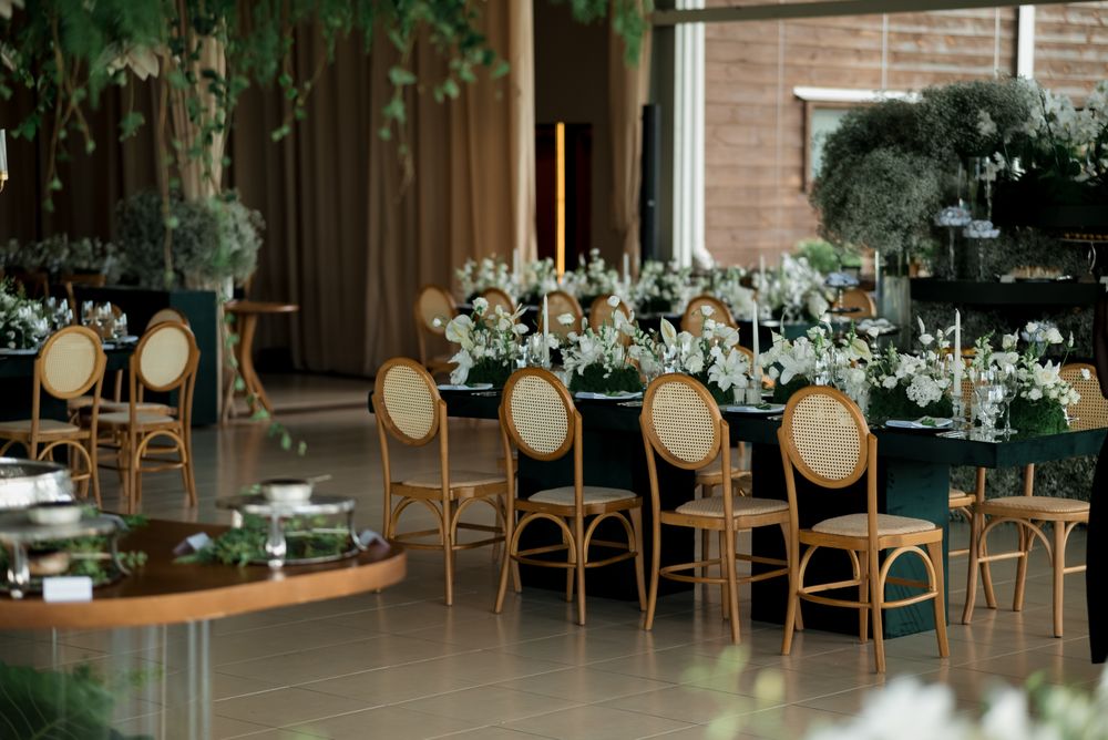 A long banquet table under hanging greenery, lined with white flowers and gold chairs