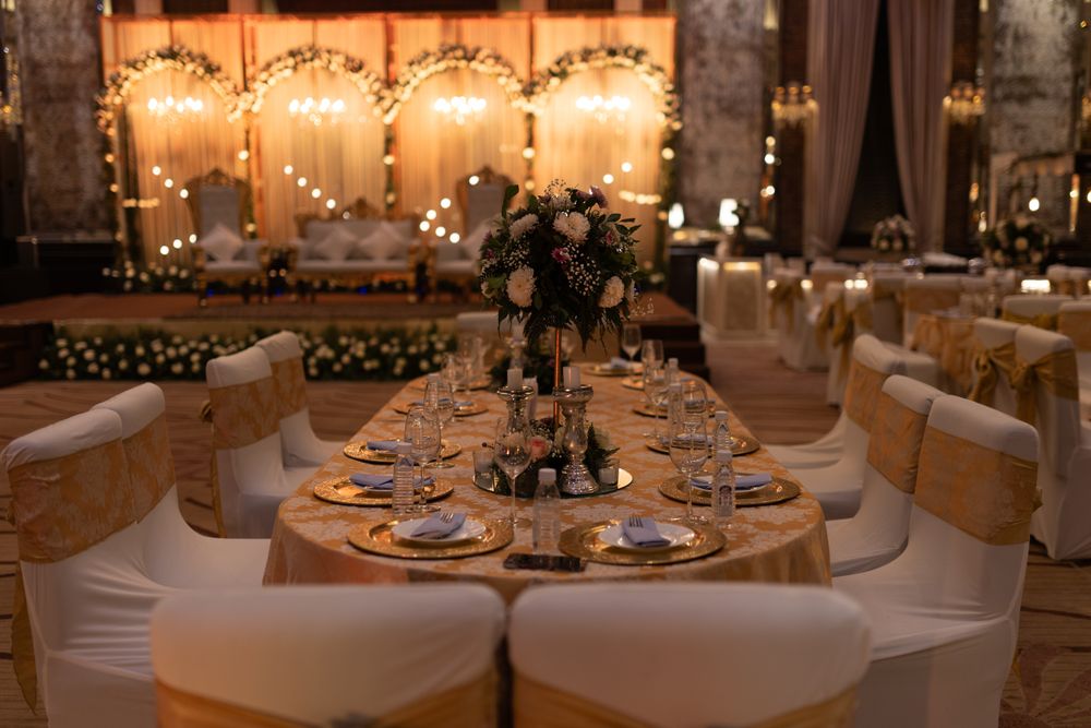 A warmly lit hall of tables with gold satin chair sashes facing an illuminated head table
