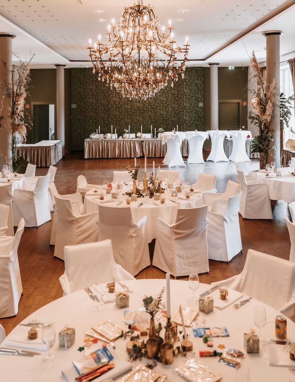 A reception hall of white-draped tables beneath a crystal chandelier