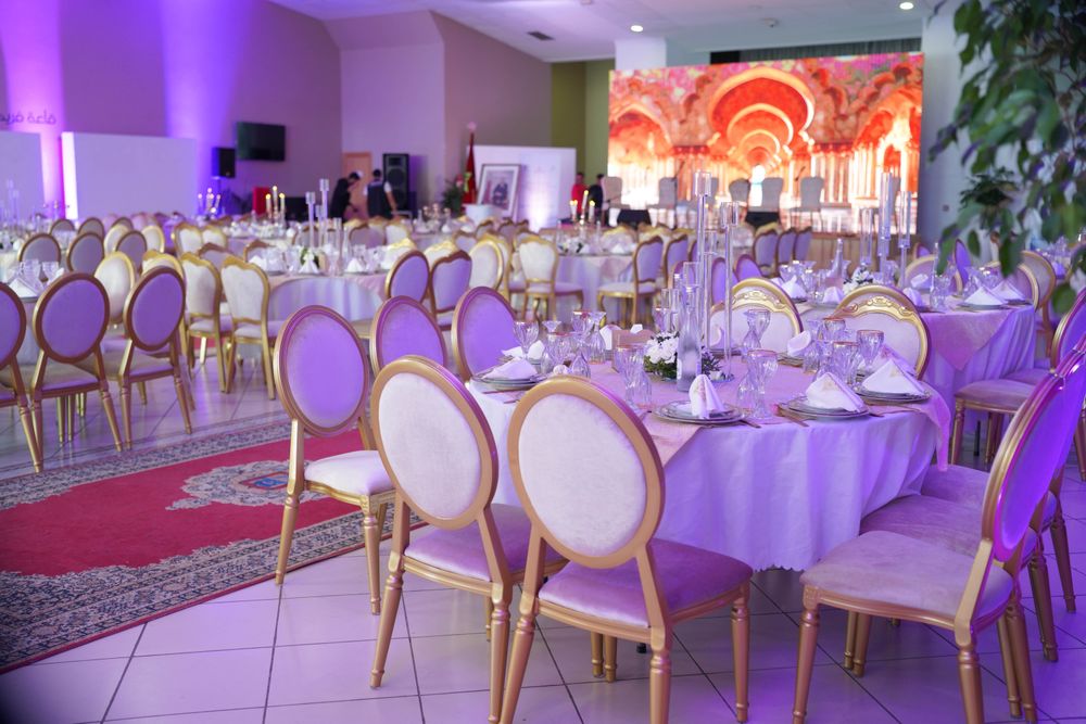 A banquet hall of round tables and gold-framed chairs washed in purple light
