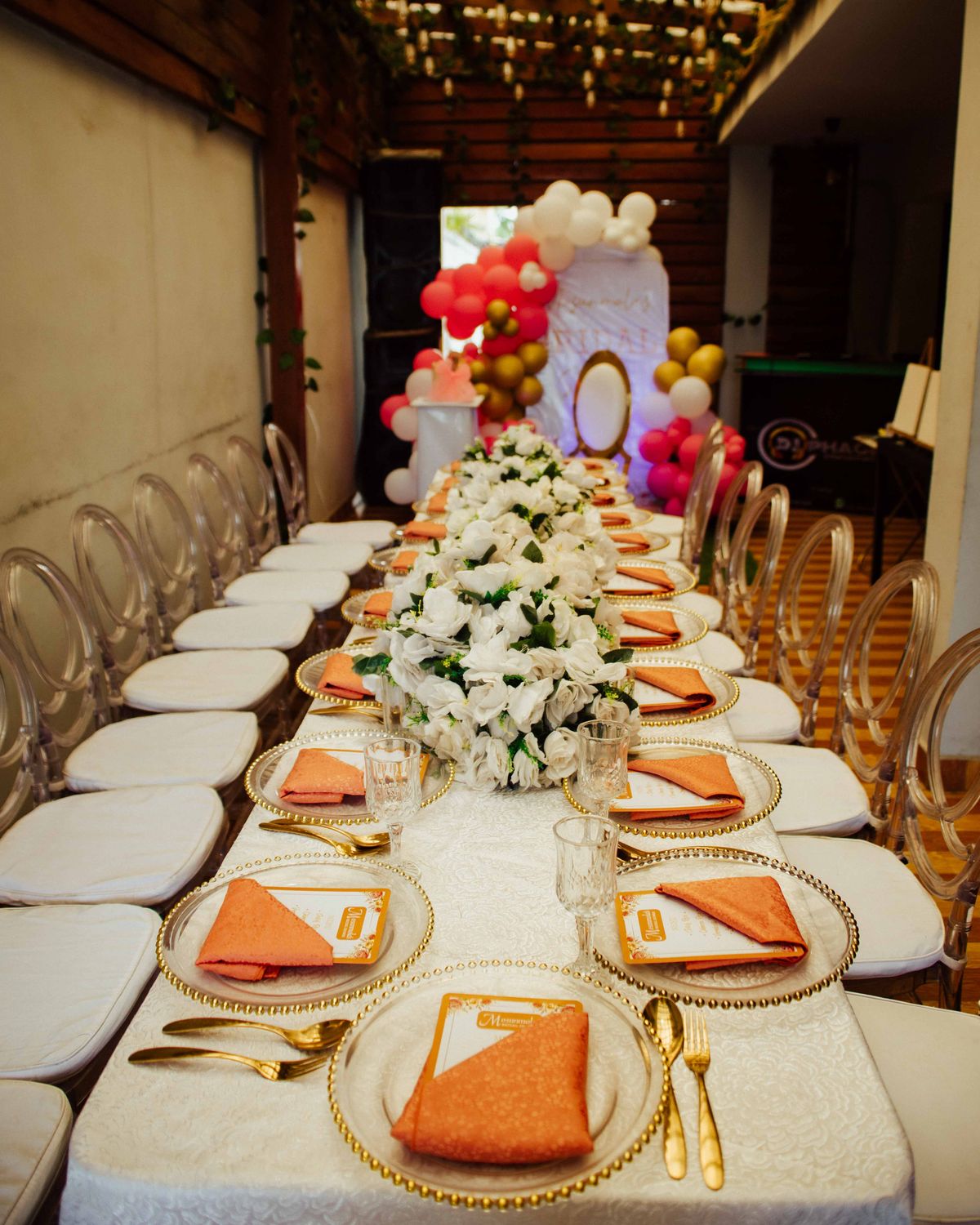 A long celebration table dressed with white flowers, gold-rimmed plates and balloons