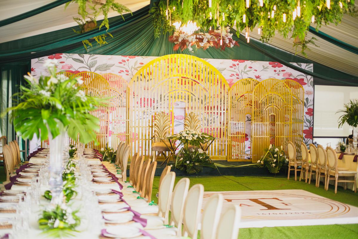 Long banquet tables leading to a floral backdrop under green draping, set for a traditional wedding